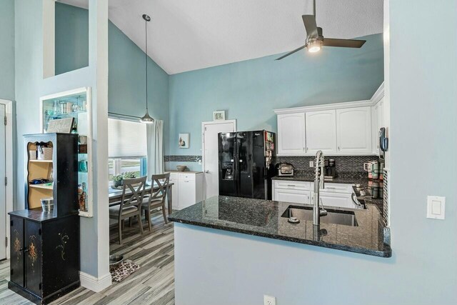 kitchen with dark stone counters, a peninsula, black fridge with ice dispenser, white cabinetry, and a sink