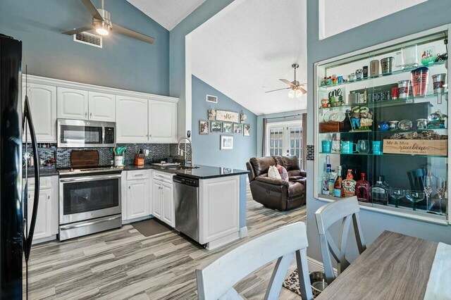 kitchen featuring dark countertops, a peninsula, stainless steel appliances, a ceiling fan, and a sink