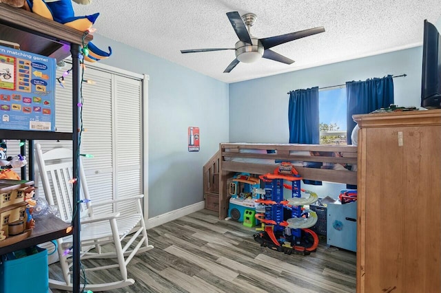 bedroom featuring a ceiling fan, a textured ceiling, wood finished floors, a closet, and baseboards