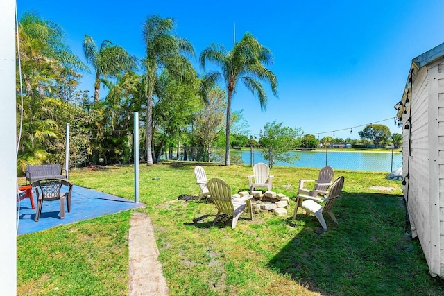 view of yard featuring a patio area, a water view, fence, and an outdoor fire pit