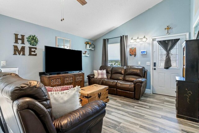 living area with baseboards, a ceiling fan, light wood-type flooring, and lofted ceiling