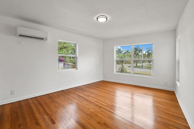 spare room featuring an AC wall unit, wood finished floors, and baseboards