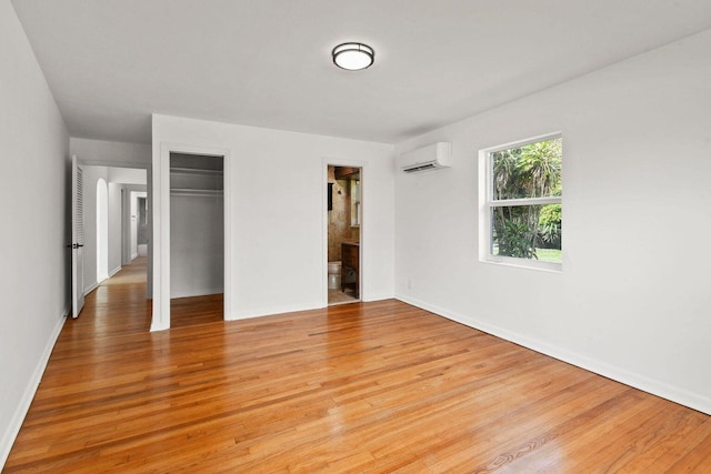 unfurnished bedroom with a closet, a wall mounted air conditioner, connected bathroom, and light wood-style flooring