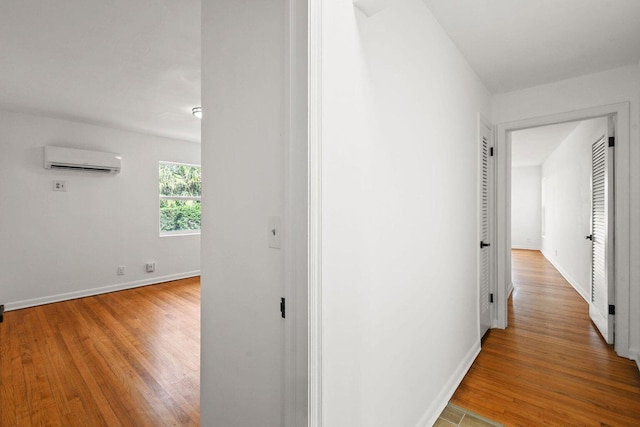 hallway featuring a wall unit AC, light wood-style flooring, and baseboards