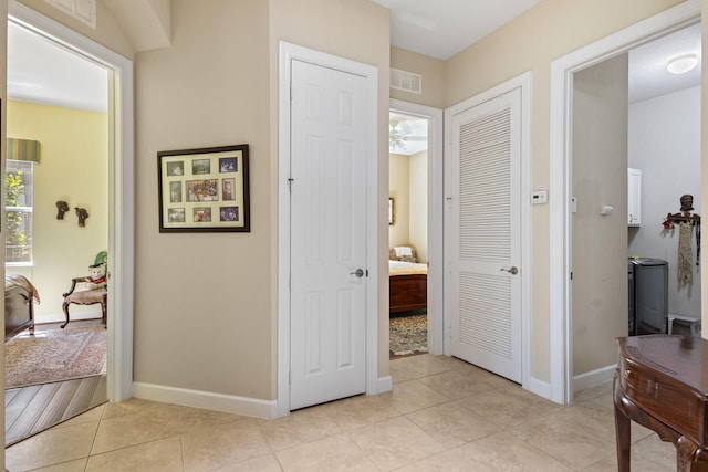 corridor with baseboards, visible vents, and light tile patterned floors