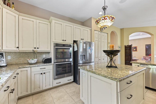 kitchen featuring tasteful backsplash, arched walkways, appliances with stainless steel finishes, a center island, and light tile patterned floors