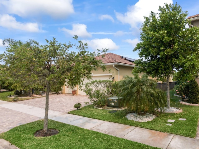 view of front of property featuring stucco siding, an attached garage, a tiled roof, decorative driveway, and a front lawn