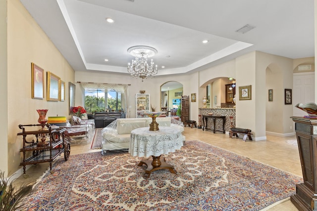 living area featuring a tray ceiling, baseboards, visible vents, and arched walkways