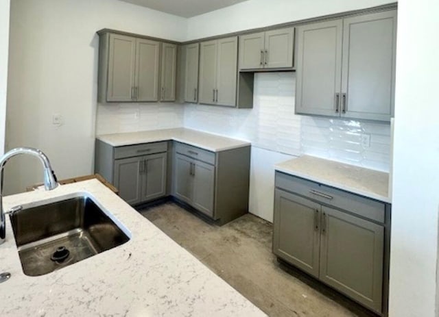 kitchen featuring tasteful backsplash, gray cabinetry, light stone countertops, and a sink