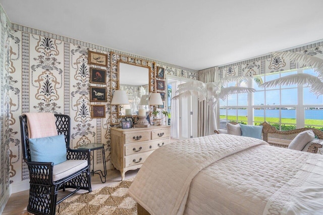 bedroom with wood finished floors, a water view, and wallpapered walls