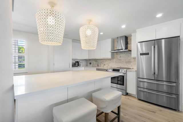 kitchen with a chandelier, white cabinetry, appliances with stainless steel finishes, decorative backsplash, and wall chimney exhaust hood