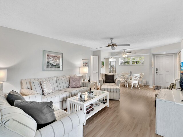 living area featuring light wood-style floors, a textured ceiling, baseboards, and a ceiling fan