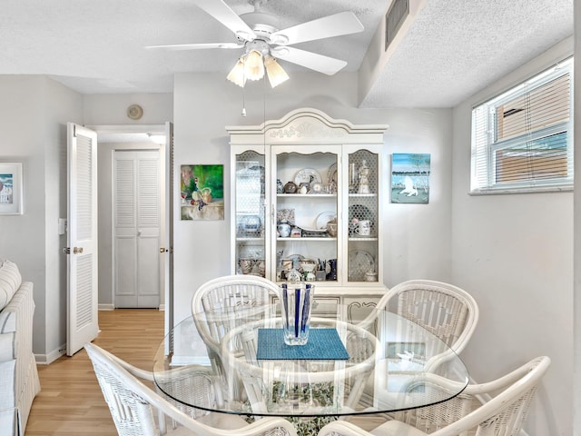 dining space with baseboards, visible vents, ceiling fan, a textured ceiling, and light wood-type flooring