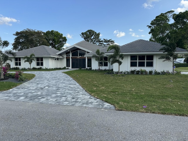 ranch-style home featuring a tile roof, a front lawn, decorative driveway, and stucco siding