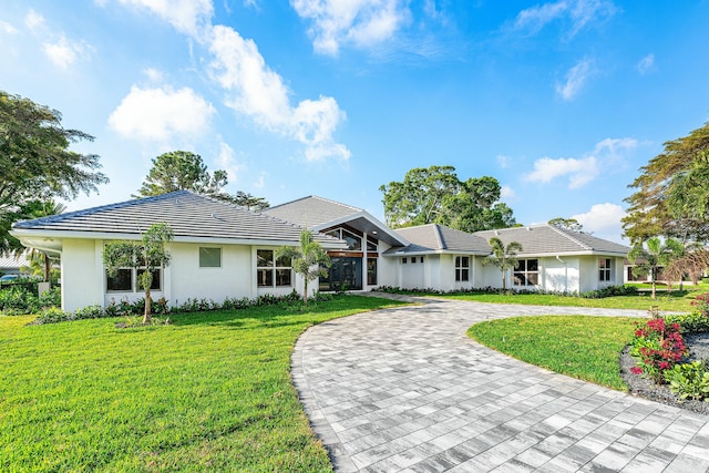 ranch-style home with a front yard, a tiled roof, decorative driveway, and stucco siding