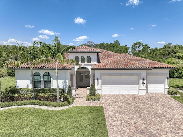 mediterranean / spanish-style house with a garage, decorative driveway, french doors, a front yard, and stucco siding