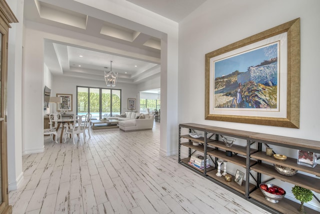 hallway featuring recessed lighting, a raised ceiling, an inviting chandelier, wood finished floors, and baseboards