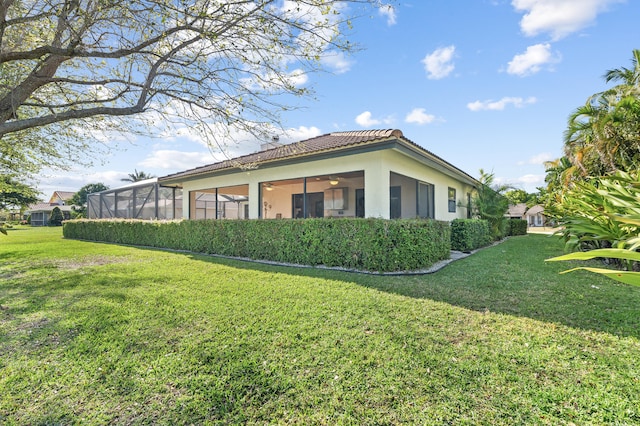 view of side of property with a yard, a tile roof, ceiling fan, and stucco siding