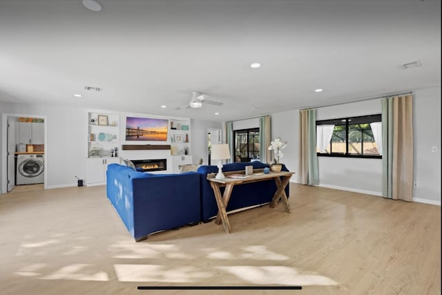 living area featuring washer / dryer, a glass covered fireplace, ceiling fan, light wood-style floors, and recessed lighting