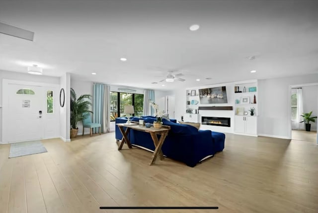 living area featuring light wood finished floors, recessed lighting, a ceiling fan, a glass covered fireplace, and baseboards