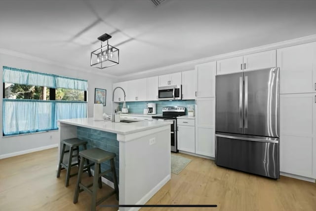 kitchen featuring light wood finished floors, appliances with stainless steel finishes, ornamental molding, white cabinetry, and a sink