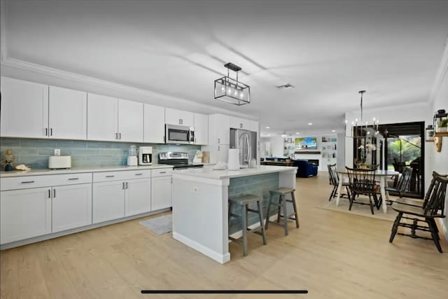 kitchen featuring light wood finished floors, ornamental molding, stainless steel appliances, and decorative light fixtures