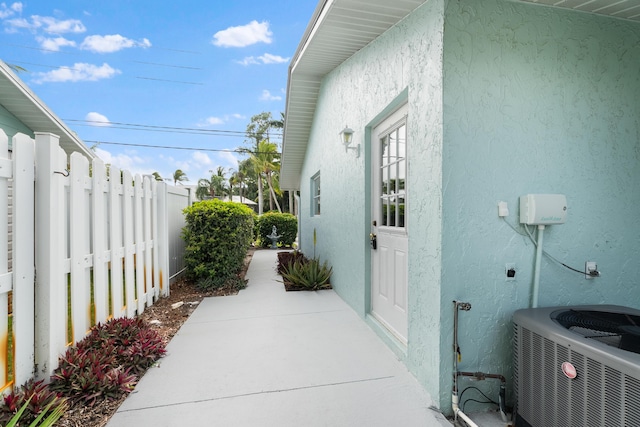 view of side of property with a patio area, stucco siding, cooling unit, and fence