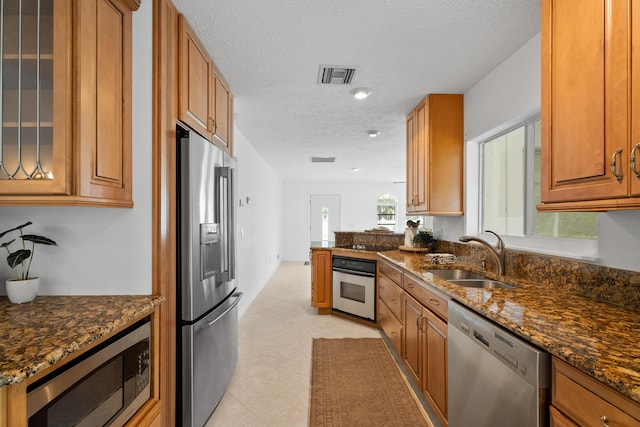 kitchen featuring brown cabinetry, visible vents, dark stone counters, a sink, and appliances with stainless steel finishes