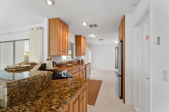 kitchen with a peninsula, dark stone counters, freestanding refrigerator, and a textured ceiling