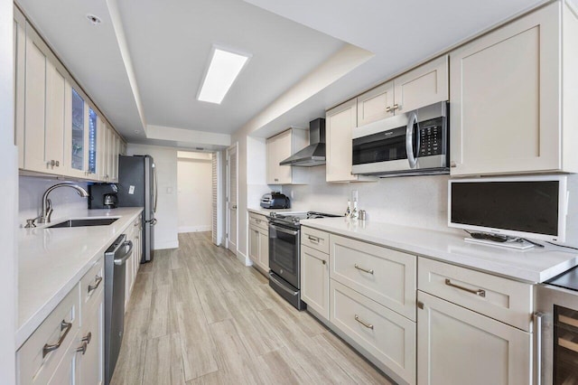 kitchen featuring tasteful backsplash, appliances with stainless steel finishes, light countertops, wall chimney range hood, and a sink