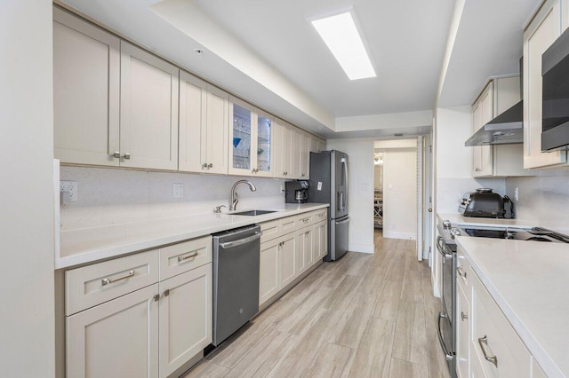 kitchen with stainless steel appliances, light wood-style flooring, decorative backsplash, a sink, and under cabinet range hood