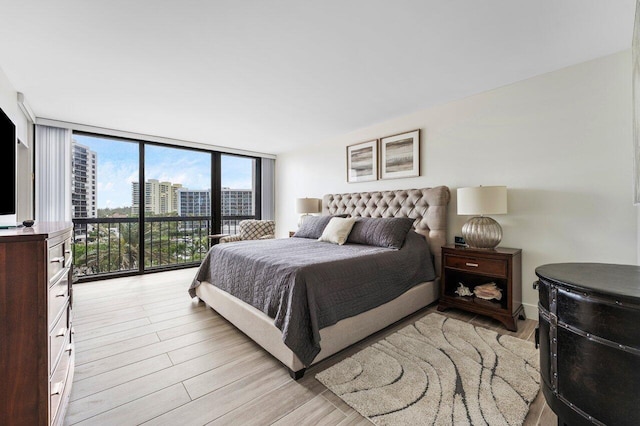 bedroom featuring a wall of windows, access to exterior, a city view, and light wood finished floors