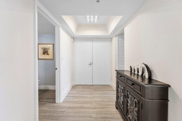 foyer featuring light wood-style floors, baseboards, and a raised ceiling