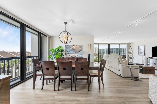 dining space with expansive windows, light wood-type flooring, rail lighting, and a notable chandelier