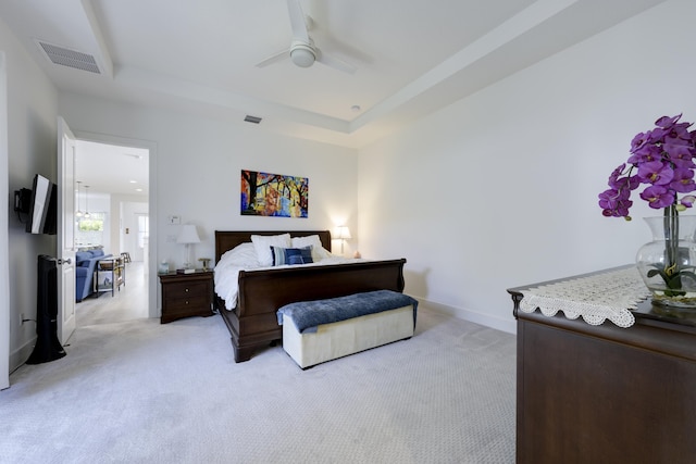 bedroom with a tray ceiling, visible vents, light carpet, and baseboards