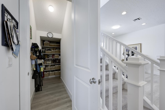 stairway featuring recessed lighting, visible vents, a textured ceiling, and wood finished floors