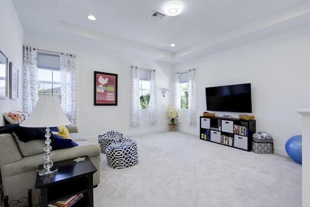 living area with a tray ceiling, visible vents, and carpet