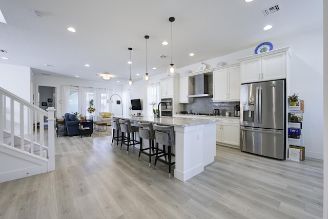 kitchen with stainless steel appliances, visible vents, open floor plan, wall chimney range hood, and a kitchen bar