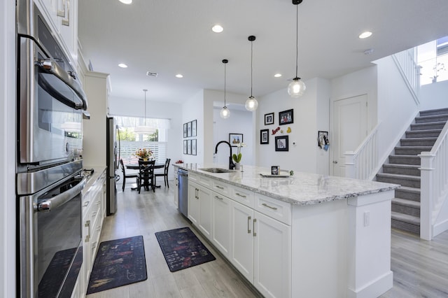 kitchen with light wood-type flooring, appliances with stainless steel finishes, a sink, and an island with sink