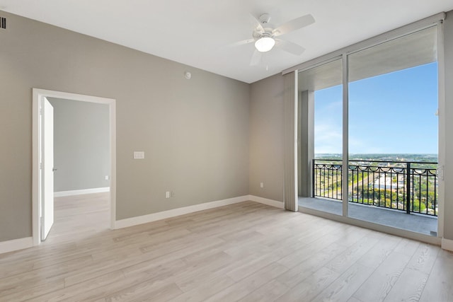 spare room featuring light wood finished floors, visible vents, baseboards, a ceiling fan, and a wall of windows