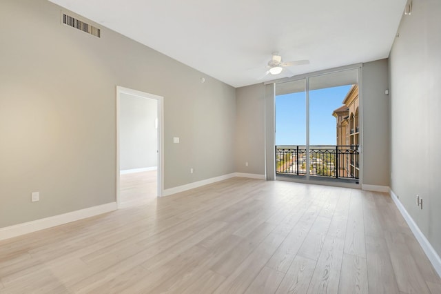 empty room featuring light wood finished floors, baseboards, visible vents, ceiling fan, and a wall of windows