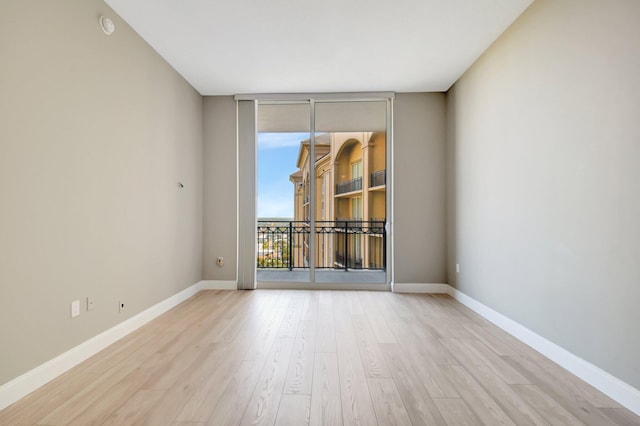 unfurnished room with baseboards, light wood finished floors, and floor to ceiling windows