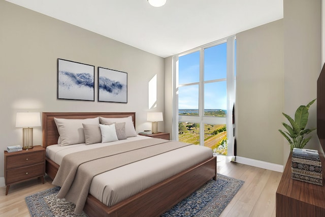 bedroom featuring light wood finished floors, a wall of windows, and baseboards