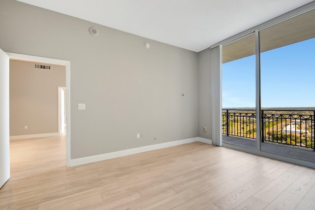 spare room featuring floor to ceiling windows, light wood-style flooring, and baseboards