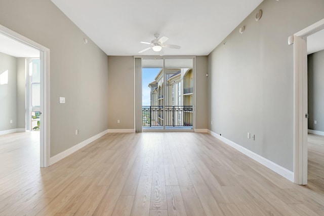 empty room featuring expansive windows, ceiling fan, light wood-style flooring, and baseboards