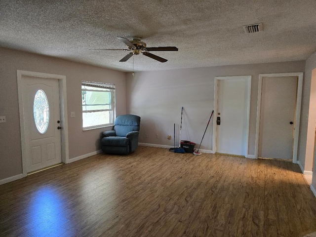 foyer featuring ceiling fan, a textured ceiling, wood finished floors, visible vents, and baseboards