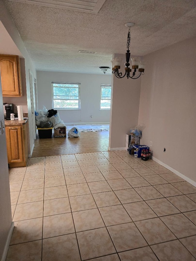 unfurnished dining area featuring light tile patterned flooring, a notable chandelier, a textured ceiling, and baseboards