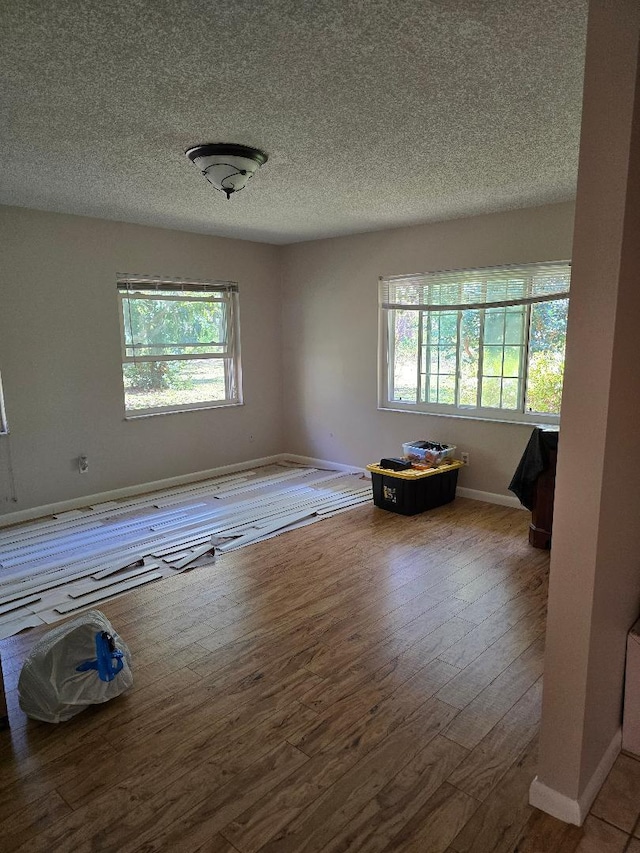 spare room featuring a textured ceiling, hardwood / wood-style flooring, and baseboards