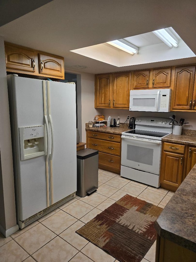 kitchen featuring dark countertops, white appliances, light tile patterned floors, and brown cabinets