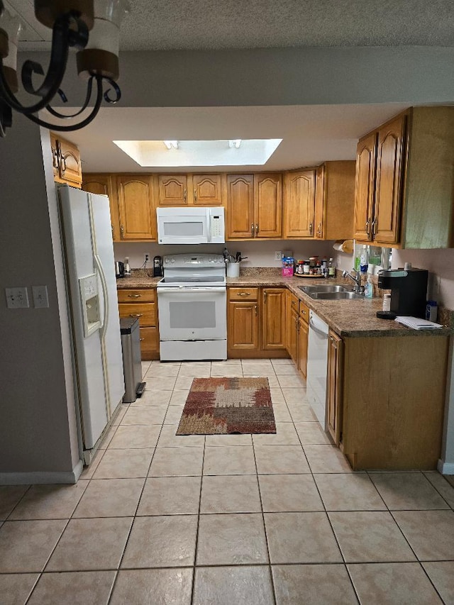 kitchen with light tile patterned floors, white appliances, a skylight, a sink, and brown cabinetry